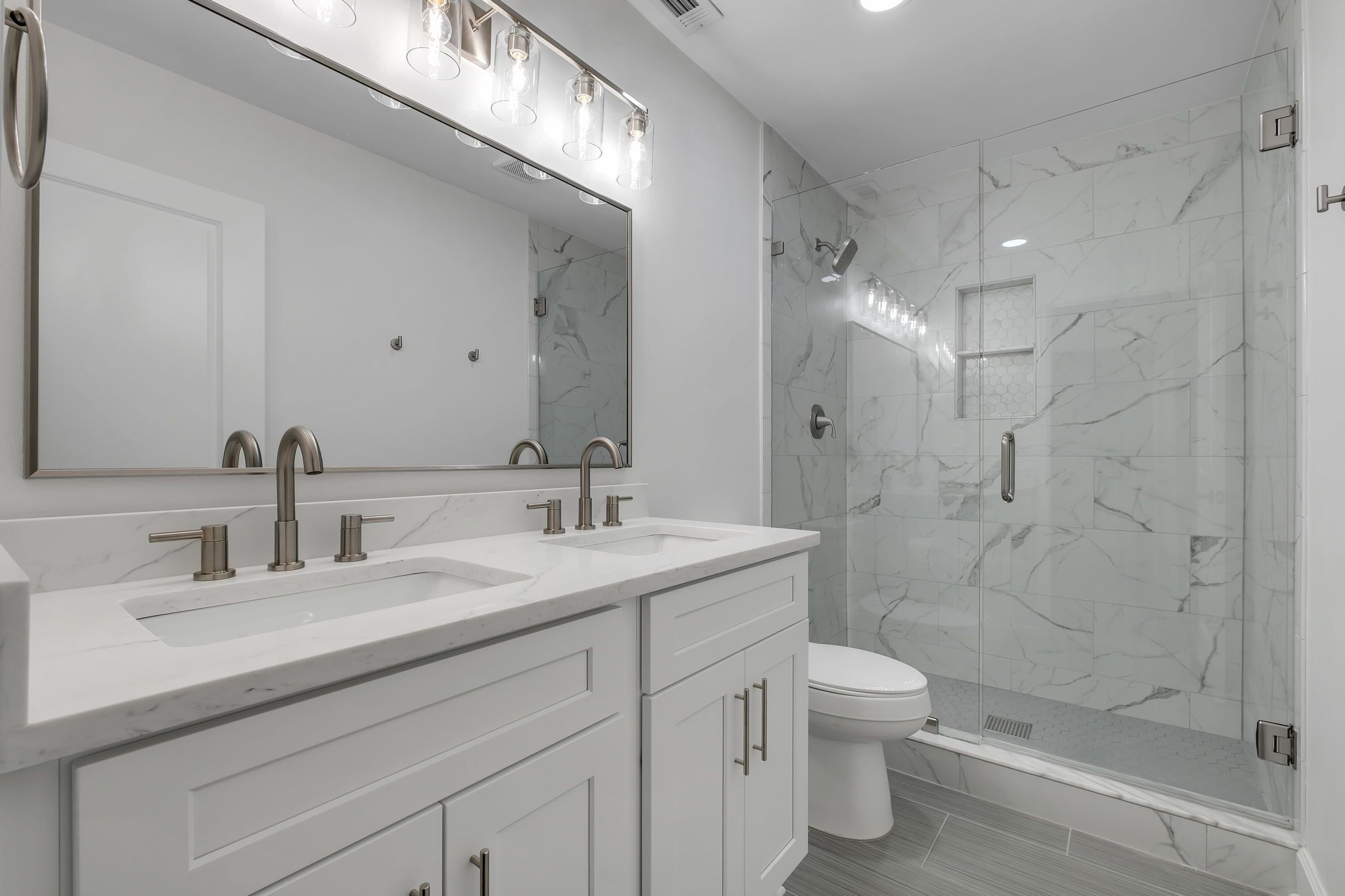Primary bathroom with a double vanity and a glass walk-in shower in marble-look tile
