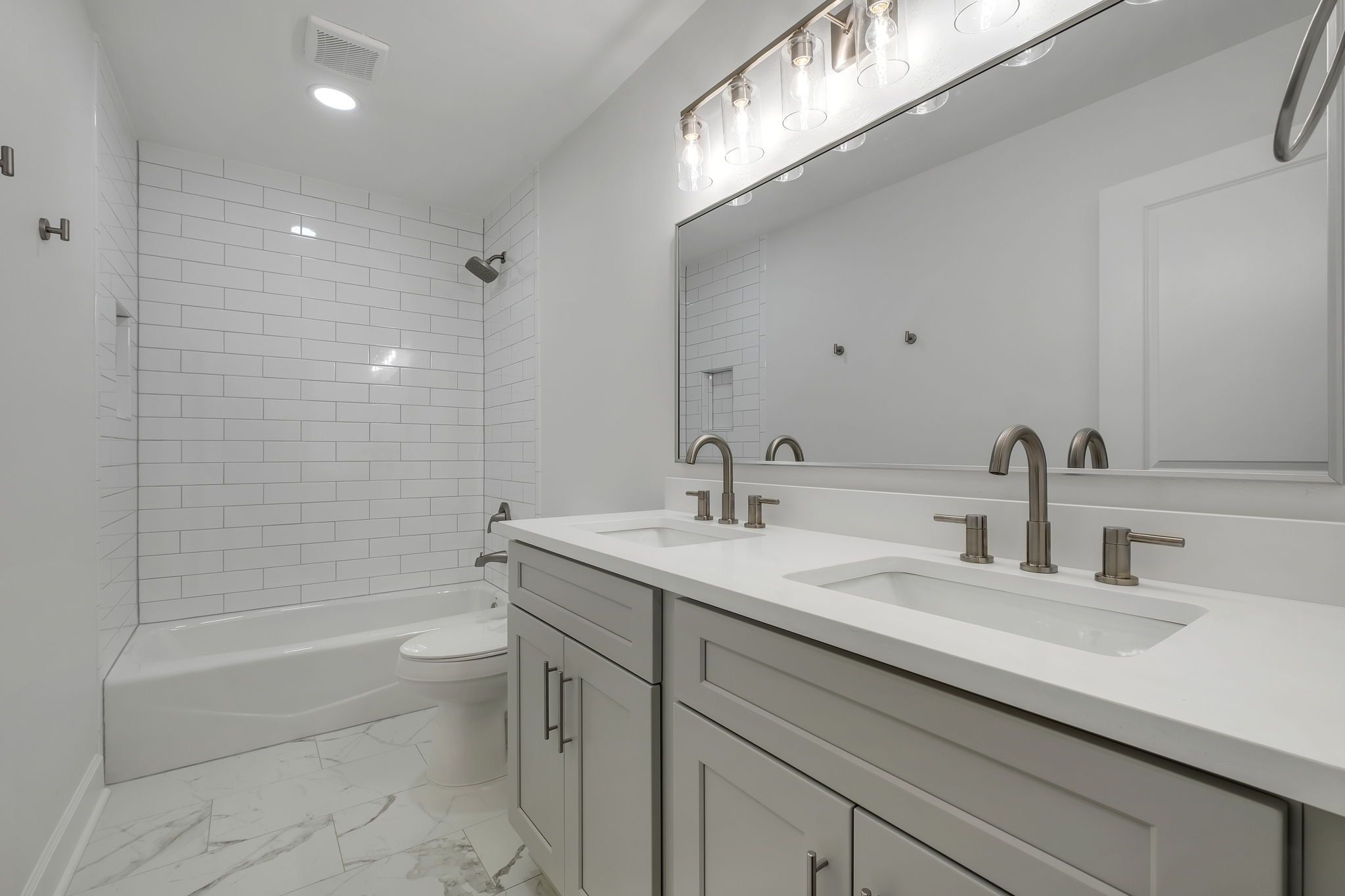 Hall bathroom with a double vanity and a subway-tiled tub and shower