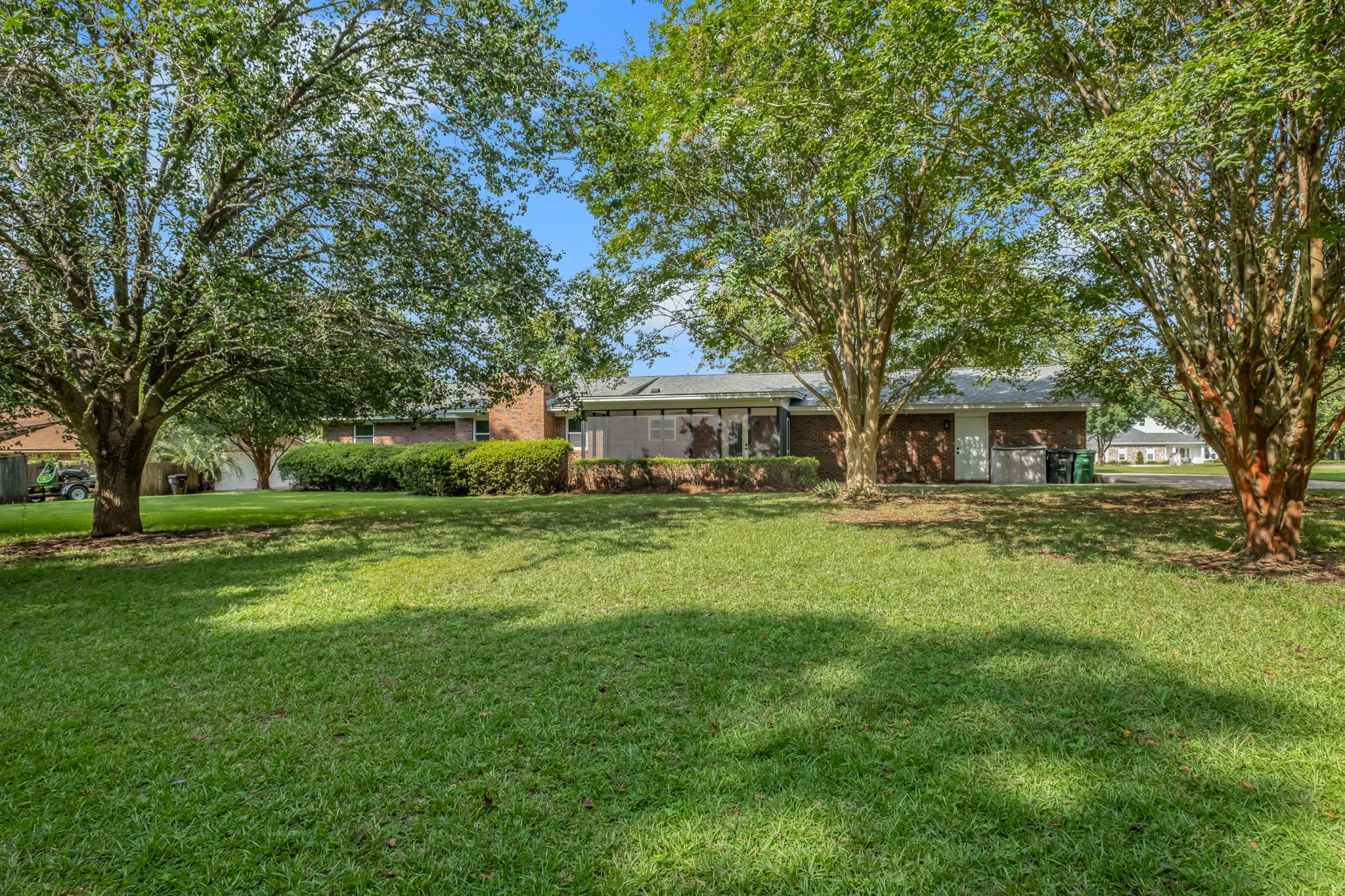 Back yard with a deep lawn and mature shade trees, the screened porch running along the back of the house