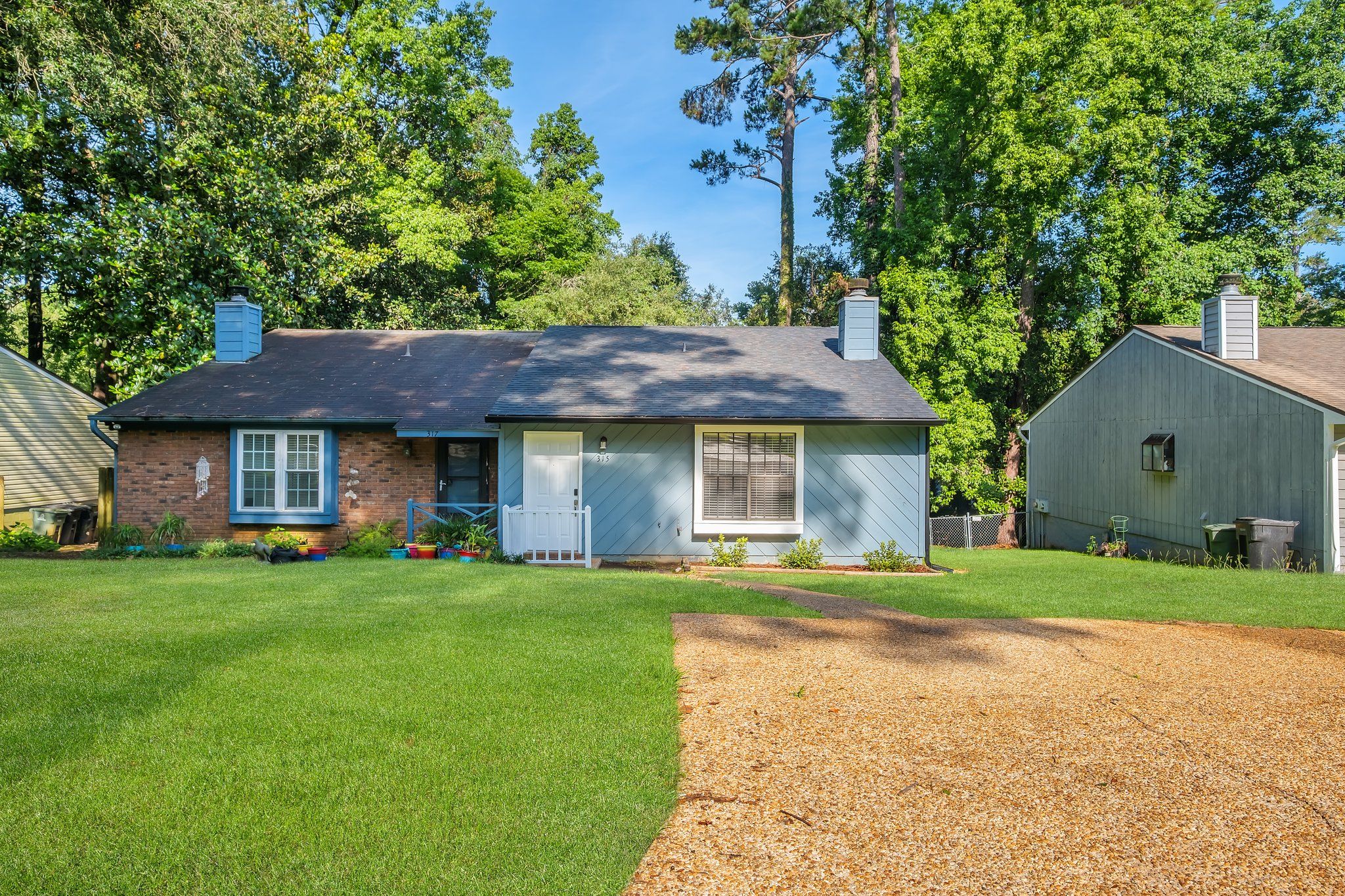 Front exterior of the Breckenridge on Park townhome: pale-blue siding over a brick base, set back behind a wide front lawn and shade trees