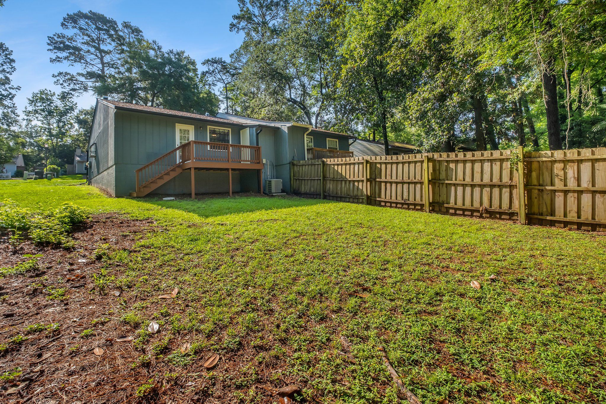 Fenced back yard with a grassy lawn and mature trees